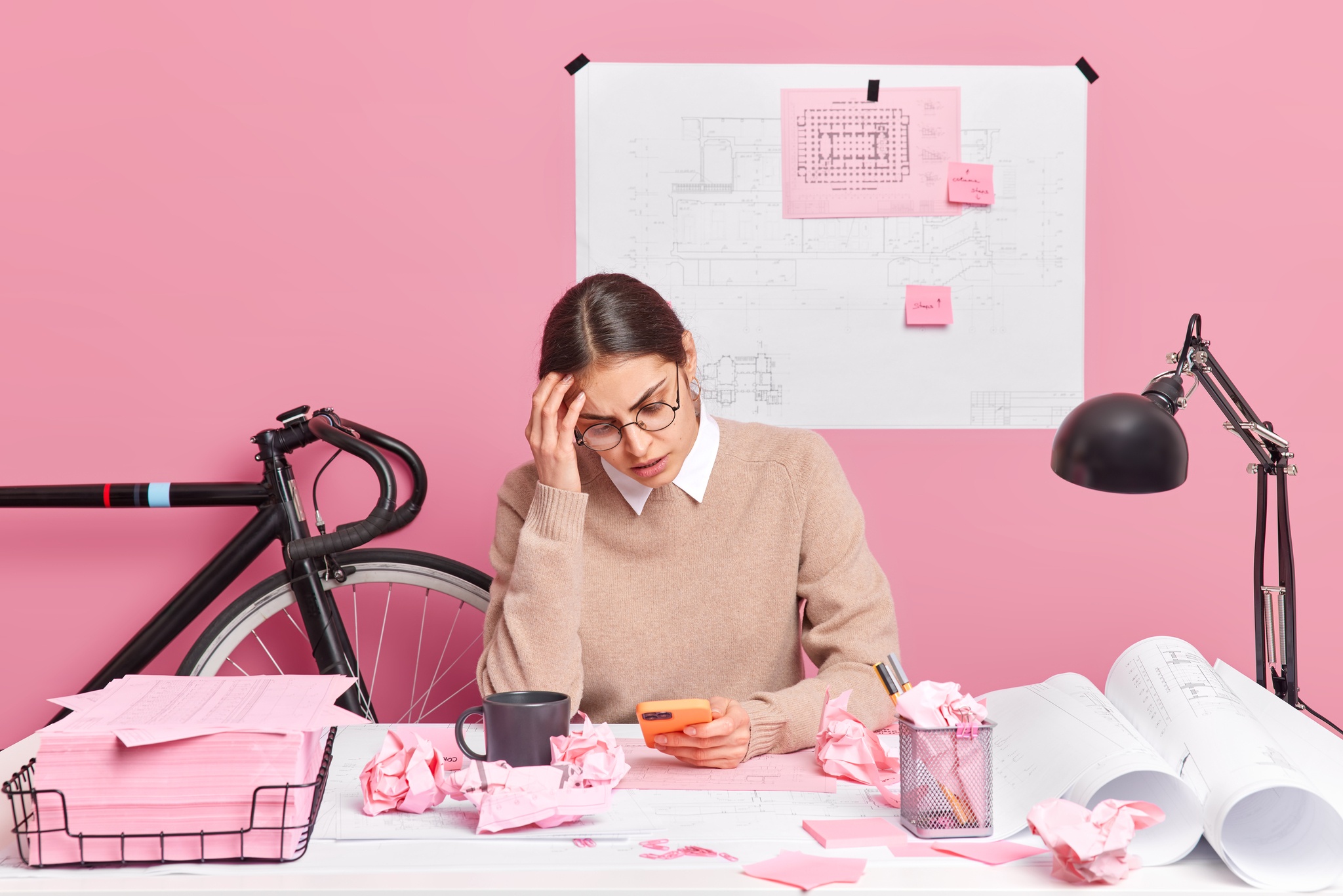 D'Aura overworked tired female architect focused smartphone has much work works architectural project makes sketches draws sketches poses coworking space against pink wall office worker 2